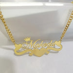 A gold nameplate necklace with the name 'Makeda' in cursive, decorated with a small crown, hearts, and a central heart, displayed on a white surface.