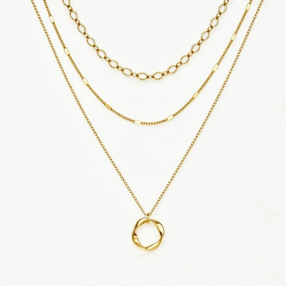 A layered gold necklace set featuring three distinct chain styles and a twisted oval pendant, displayed on a clean white background.