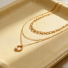 A double-strand gold necklace with a textured circular pendant, displayed on a cream-colored leather tray.