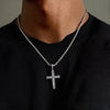Person wearing a silver cross necklace on a plain background