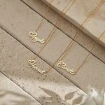 Three gold name necklaces on a stone surface