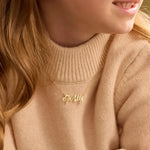 Close-up of a person wearing a beige sweater with a gold name necklace that spells 'Molly' in cursive script,