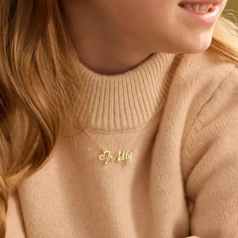 Close-up of a person wearing a beige sweater with a gold name necklace that spells 'Molly' in cursive script,
