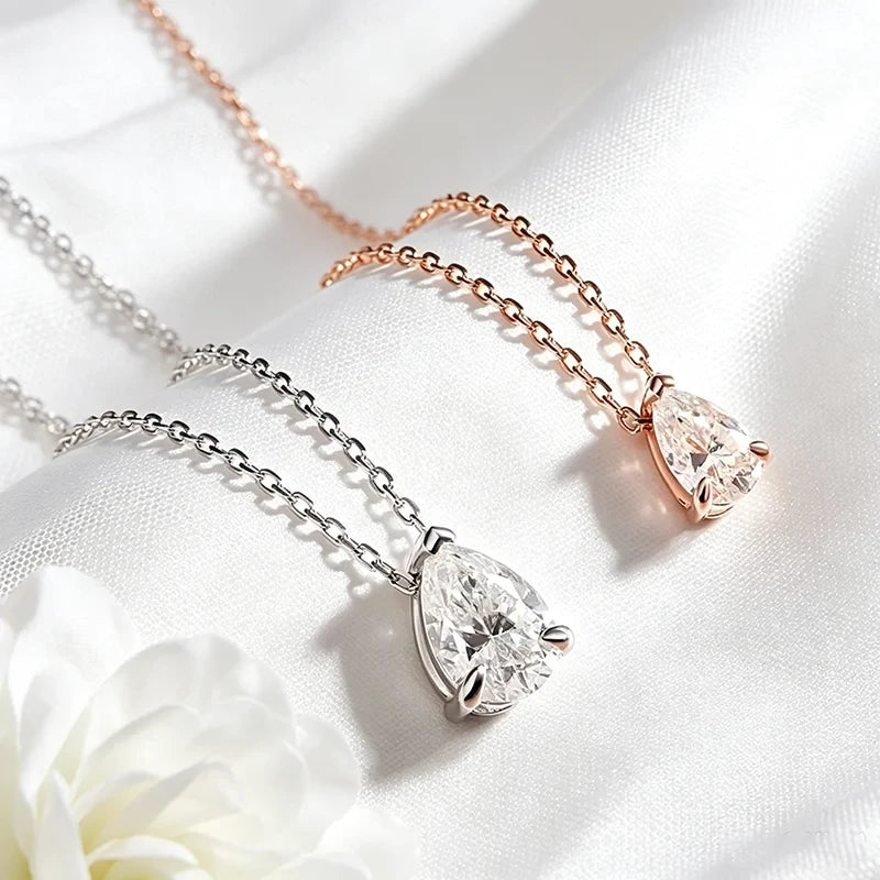 Two teardrop pendant necklaces on white satin fabric, one in silver and one in rose gold, each featuring a clear faceted gemstone.