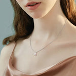 Close-up of a woman wearing a delicate silver necklace with a heart pendant against a neutral background.