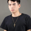 Man wearing a black t-shirt and gold necklace with a cross pendant against a gray background