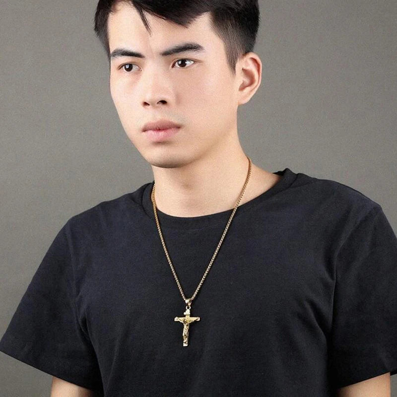 Man wearing a black t-shirt and gold necklace with a cross pendant against a gray background